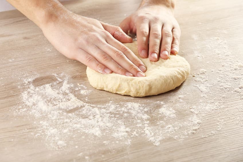 hands kneading dough on wooden surface