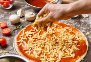 Man making the pizza, adding cheese on pizza base